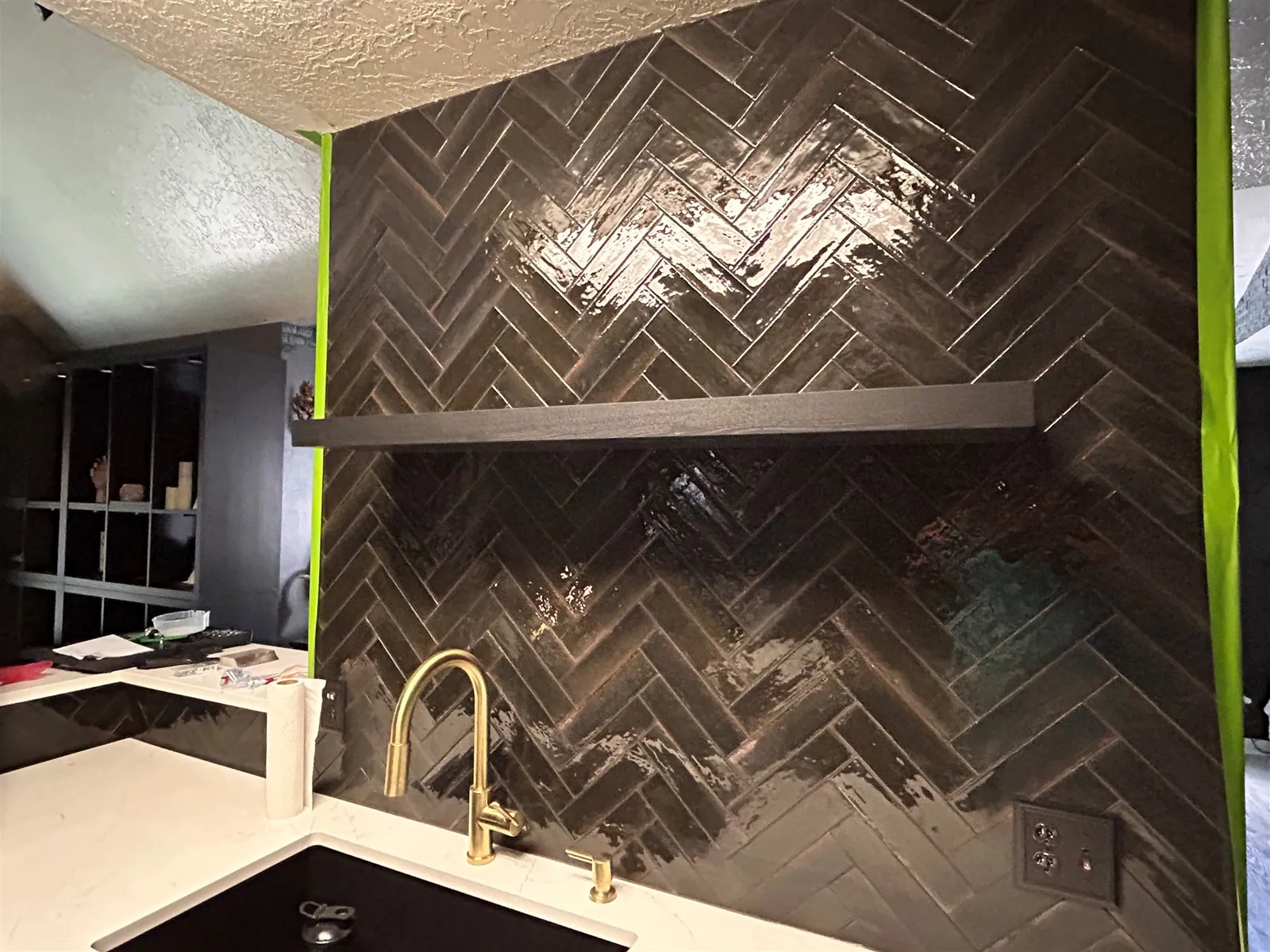 Herringbone tile backsplash installation with gold faucet