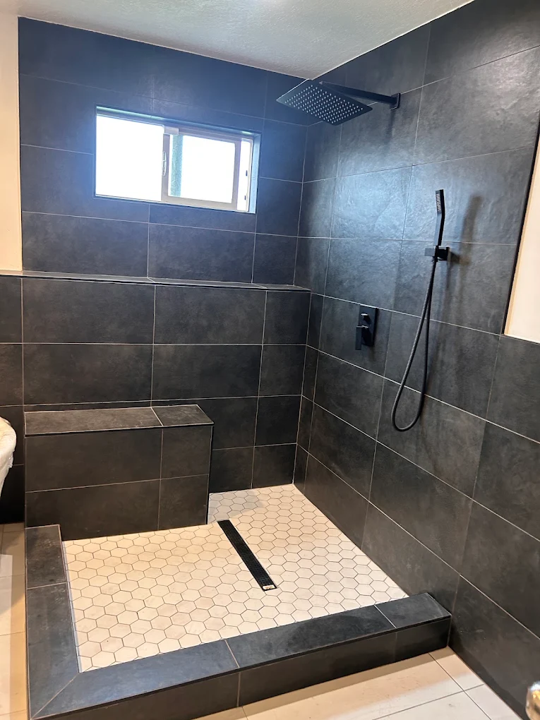 Remodeled walk-in shower with large charcoal tile, built-in bench, and hexagon tile floor