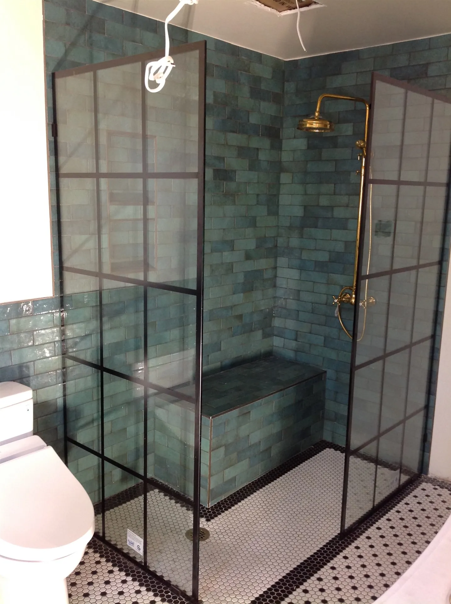 Walk-in glass shower with teal tile and penny-round floor