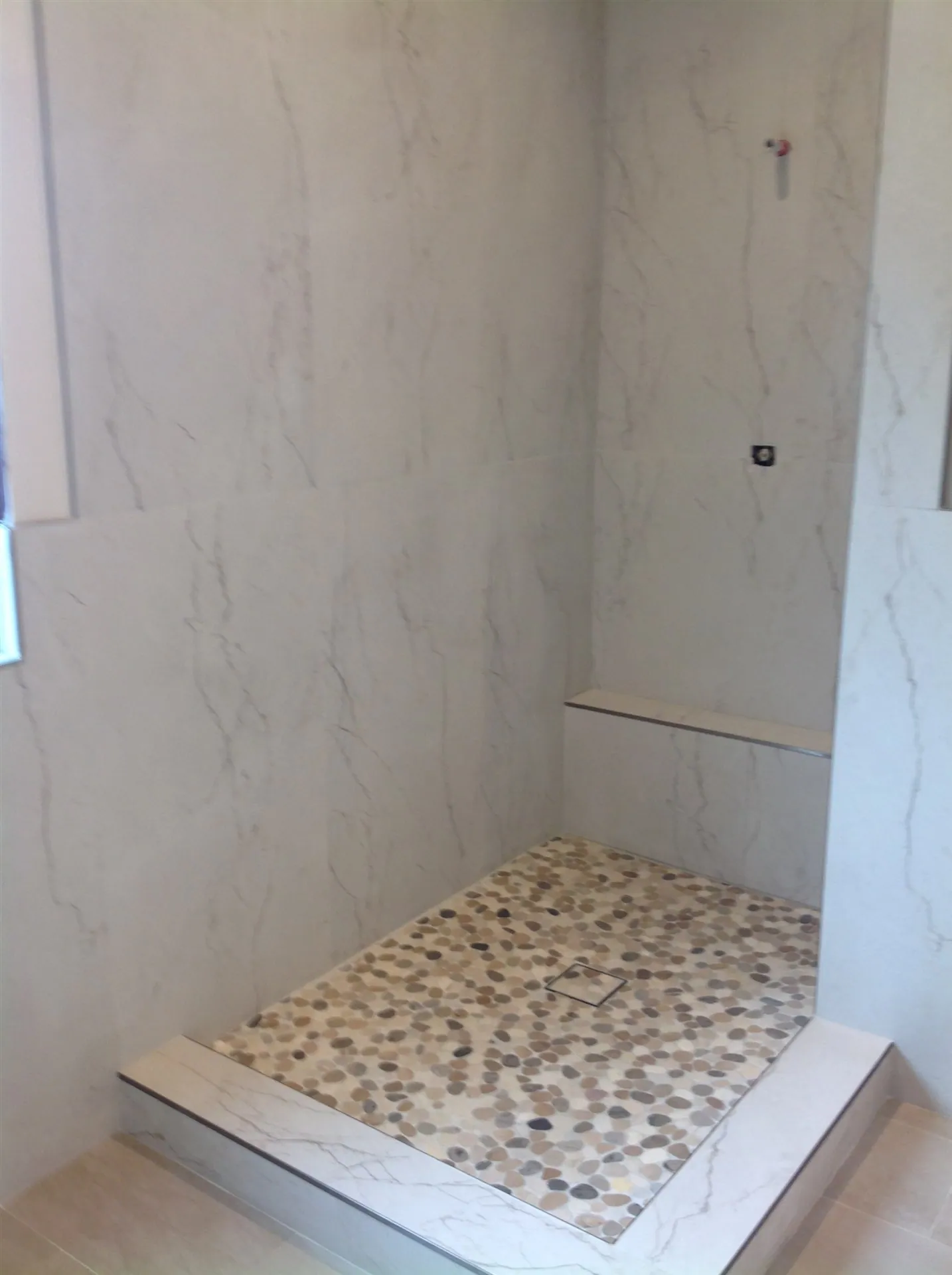 White marble-look shower with pebble tile floor