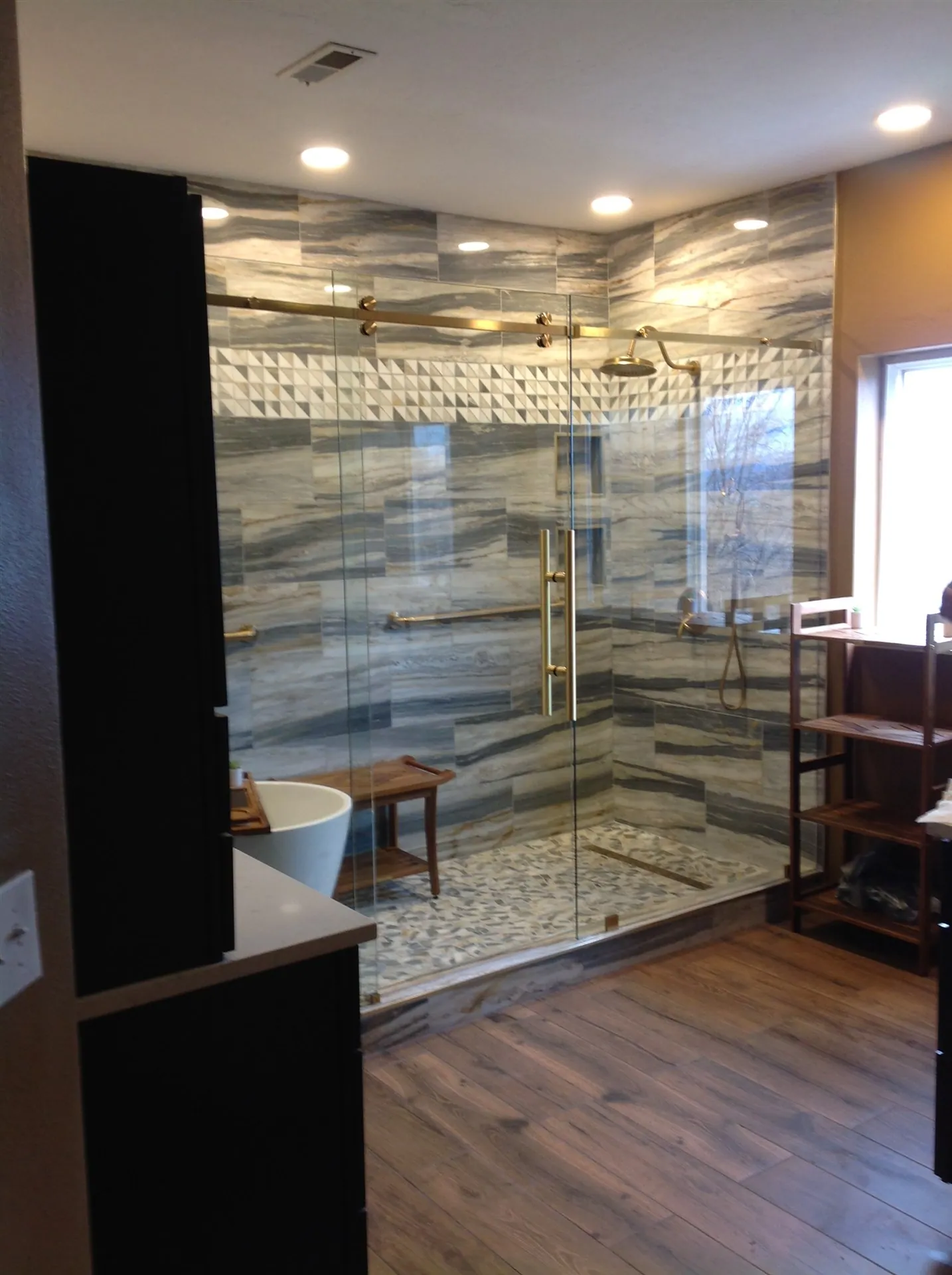 Master bathroom with book-matched stone walls and glass shower
