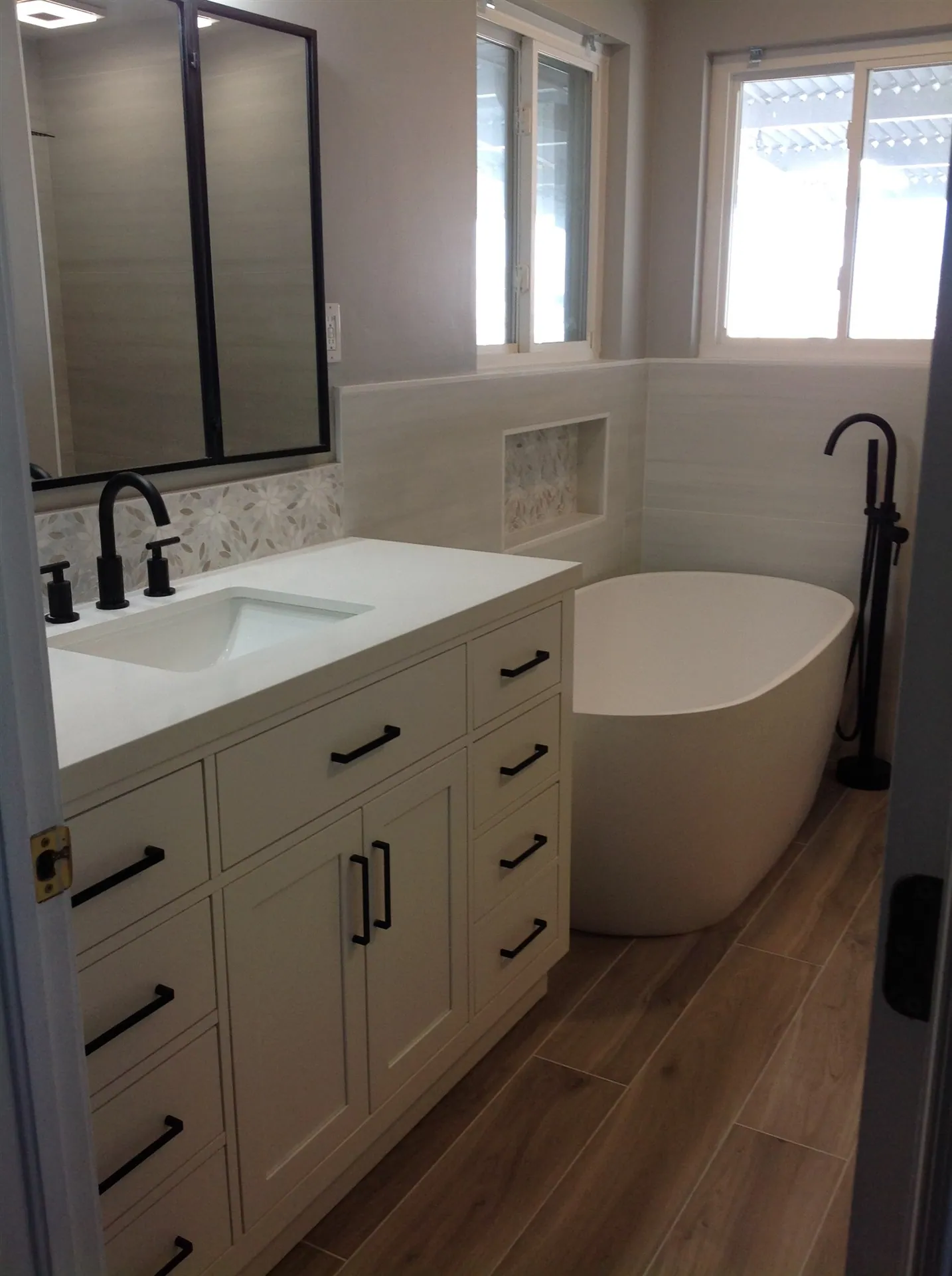 White shaker vanity with freestanding tub and wood-look floor