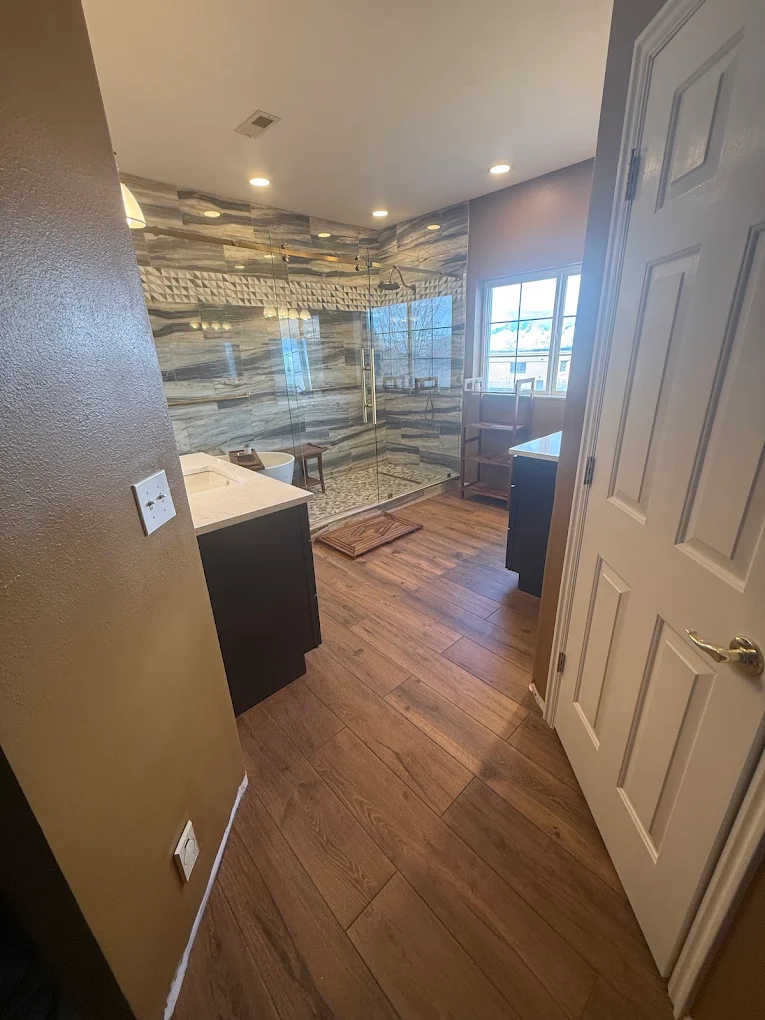 Master bathroom remodel with dual vanities, wood-look flooring, and a glass walk-in shower